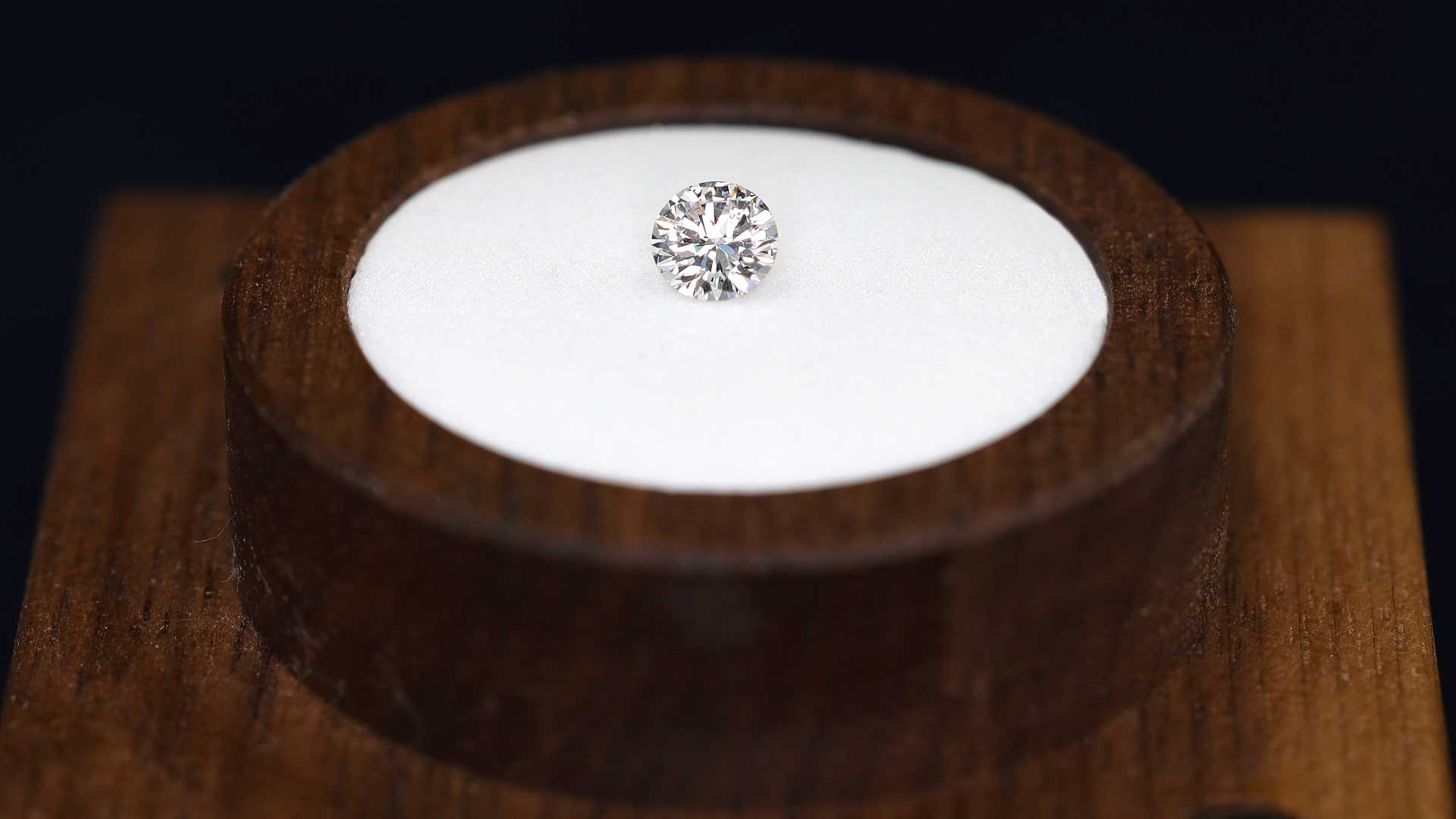 Funkelnder Erinnerungsdiamant im Brillantschliff, präsentiert auf einer runden weißen Einlage in einem Holzsockel für eine Diamantbestattung.