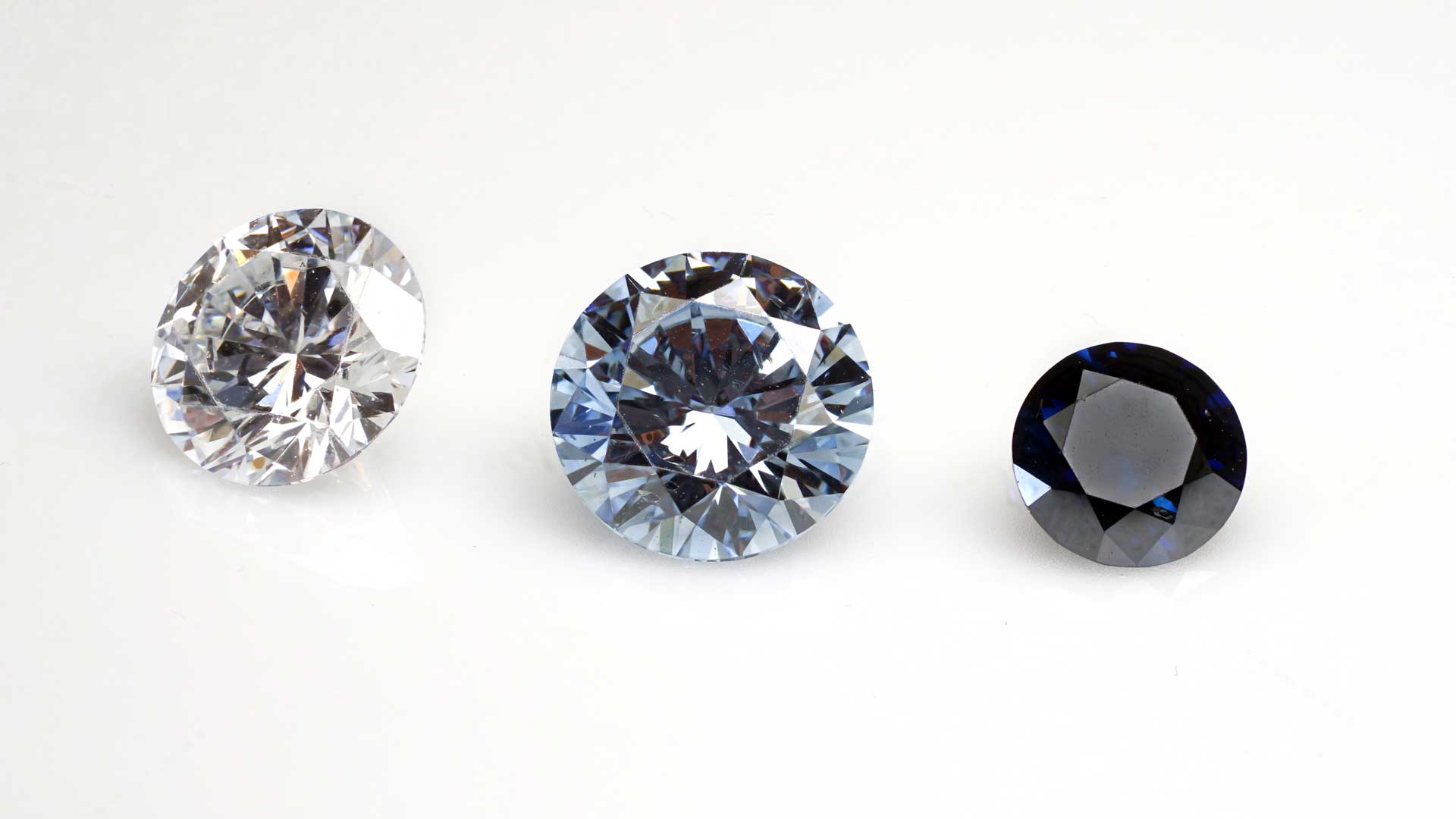 Drei kunstvoll geschliffene Erinnerungsdiamanten nebeneinander auf weißem Grund in den Farben Weiß, Hellblau und Dunkelblau für eine Diamantbestattung.