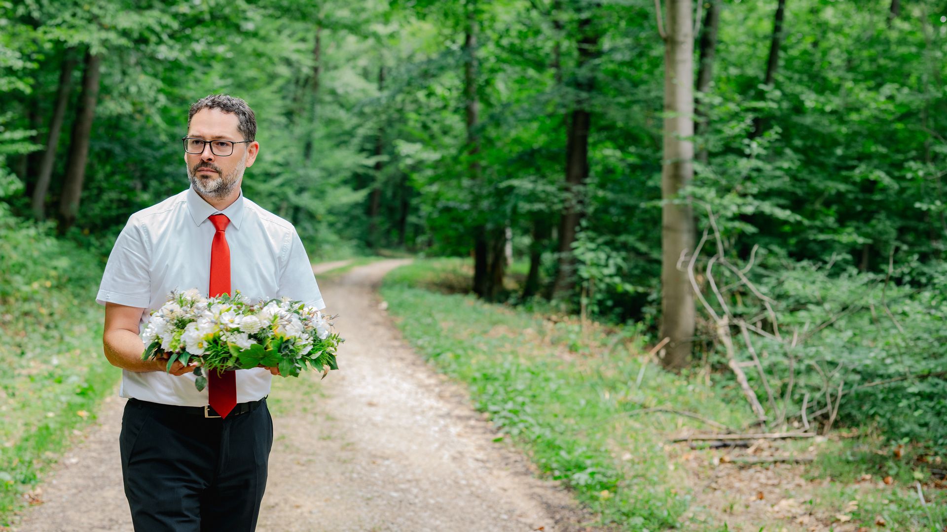 Bestatter Carsten Fezer trägt einen weißen Blumenkranz auf einem Waldweg im FriedWald Schurwald.