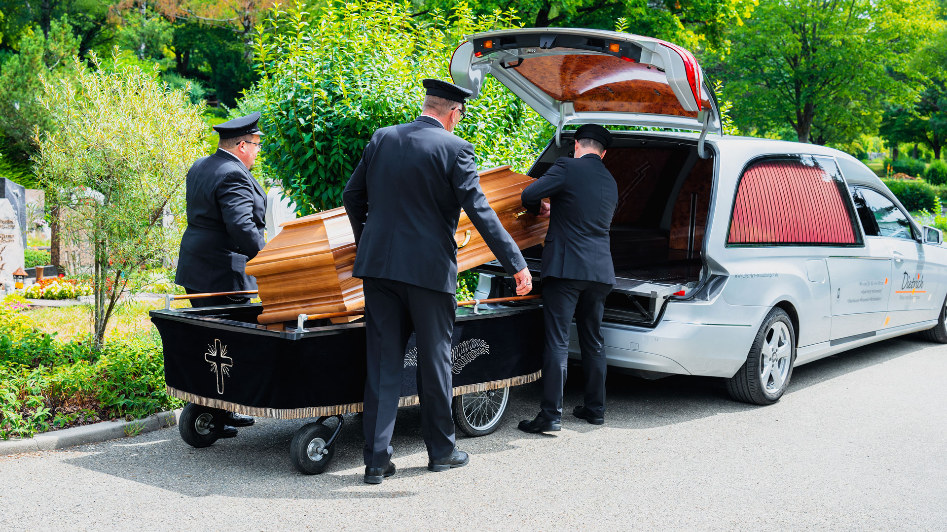 Drei Sargträger von Dietrich Haus der Bestattung heben einen Holzsarg am Friedhof Schorndorf aus einem silbernen Bestattungswagen.