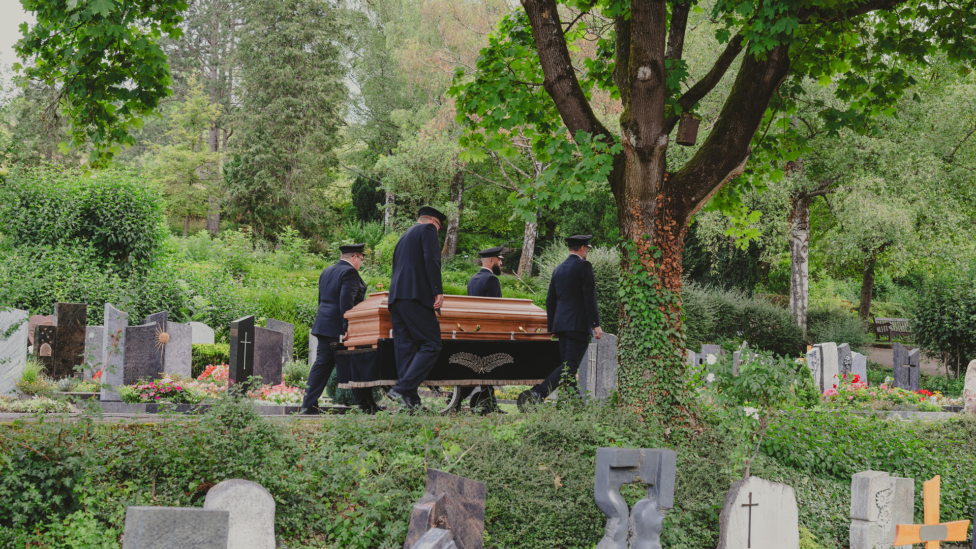 Vier Sargträger von Dietrich Bestattungen geleiten einen Holzsarg auf einem Sargwagen über den Friedhof Schorndorf.
