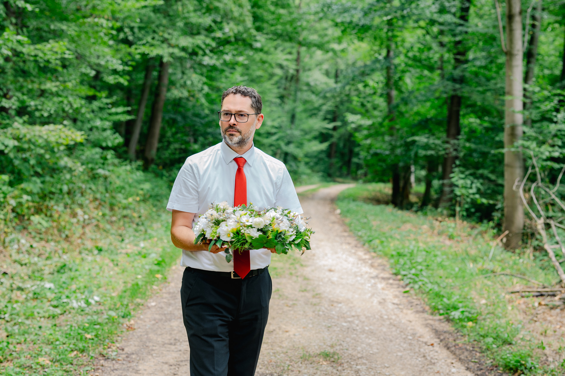 Carsten Fezer von Dietrich – Haus der Bestattung trägt einen floralen Trauerkranz auf einem Waldweg im FriedWald Schurwald.
