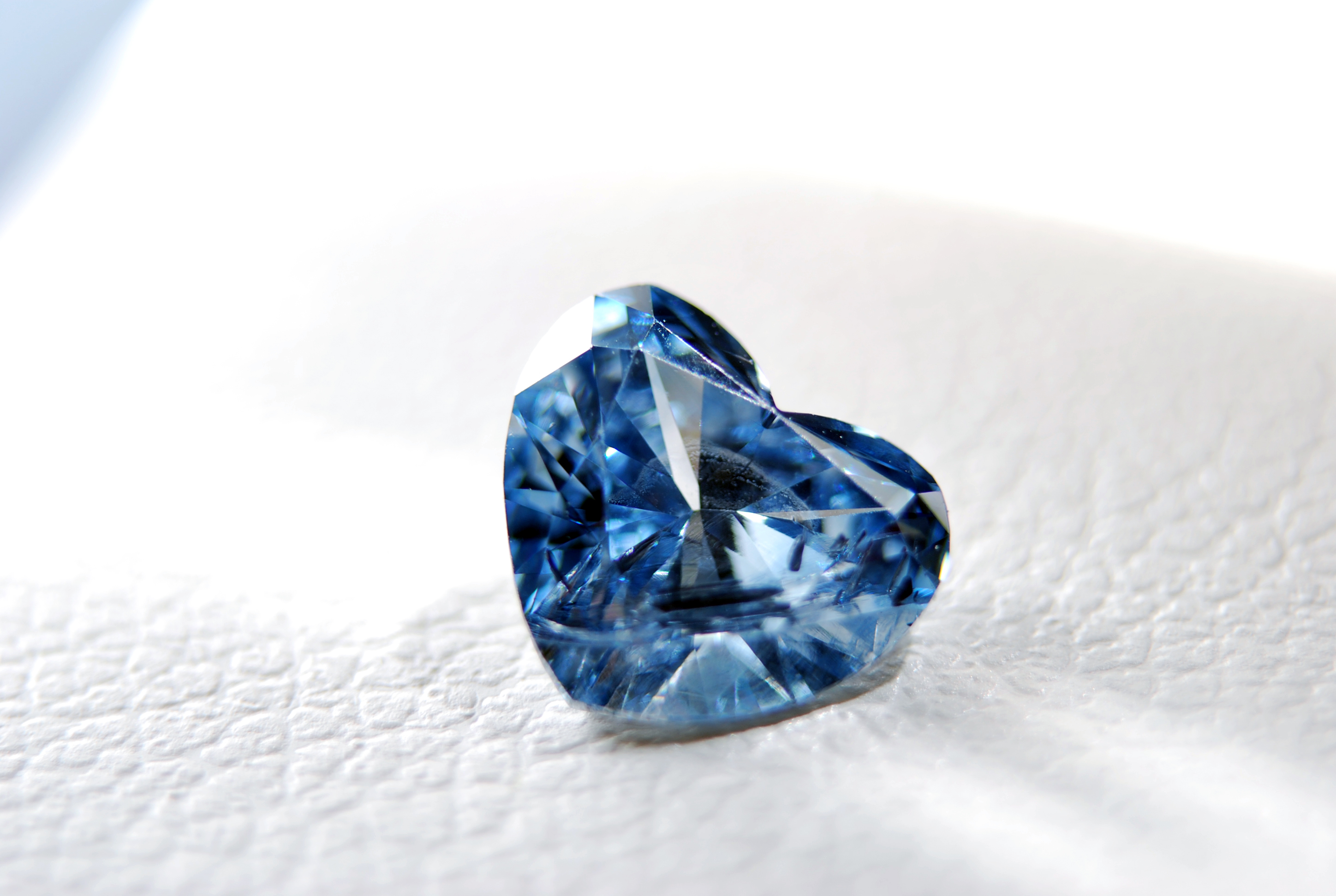 Makroaufnahme eines blau funkelnden Erinnerungsdiamanten im präzisen Herzschliff auf einem weißen, strukturierten Hintergrund für eine Diamantbestattung.